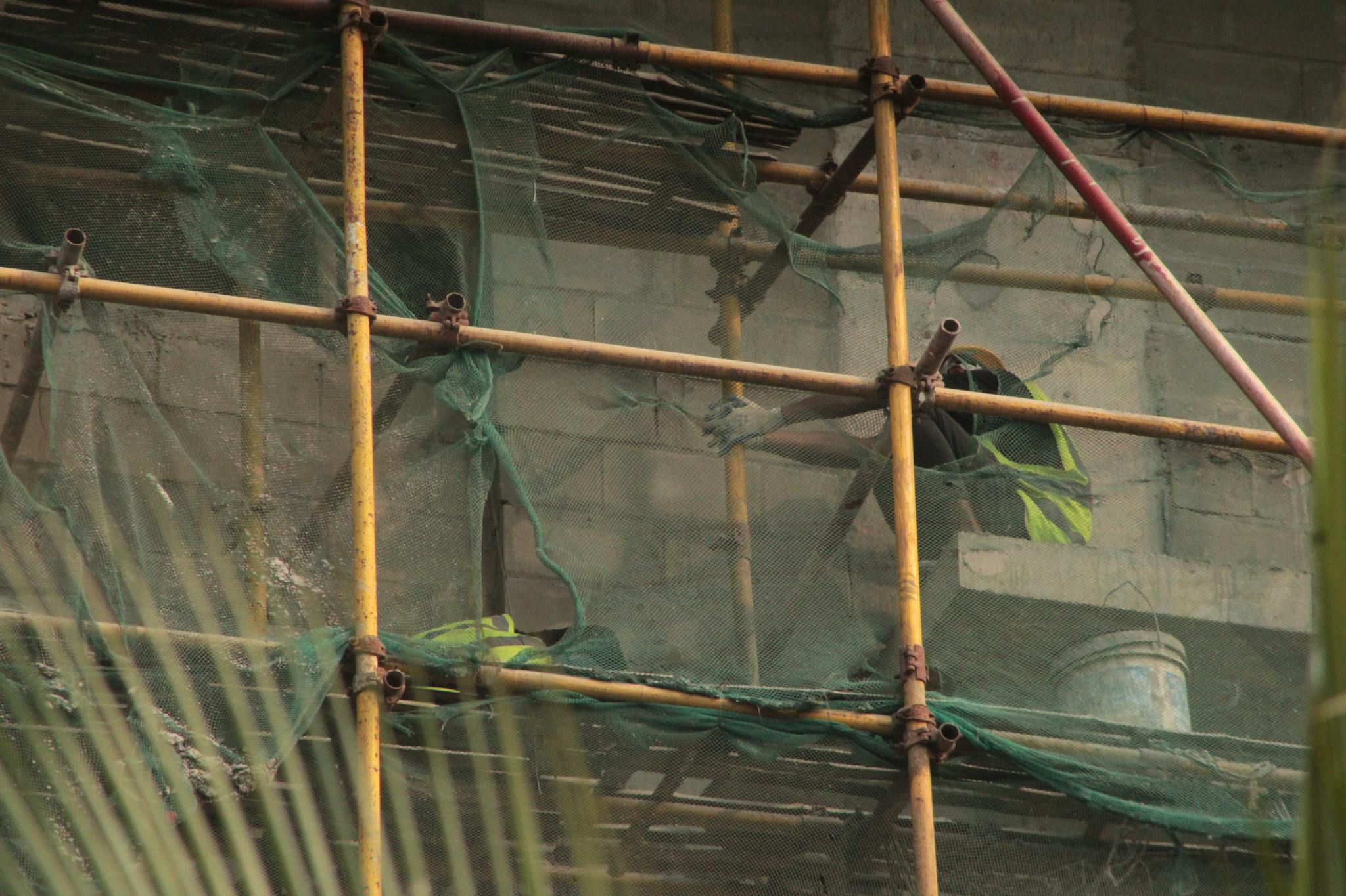 Workers on a building site, secured with scaffolding and safety netting.